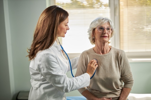Mid adult female doctor uses a stethoscope to check the heart and lungs on a senior female patient.